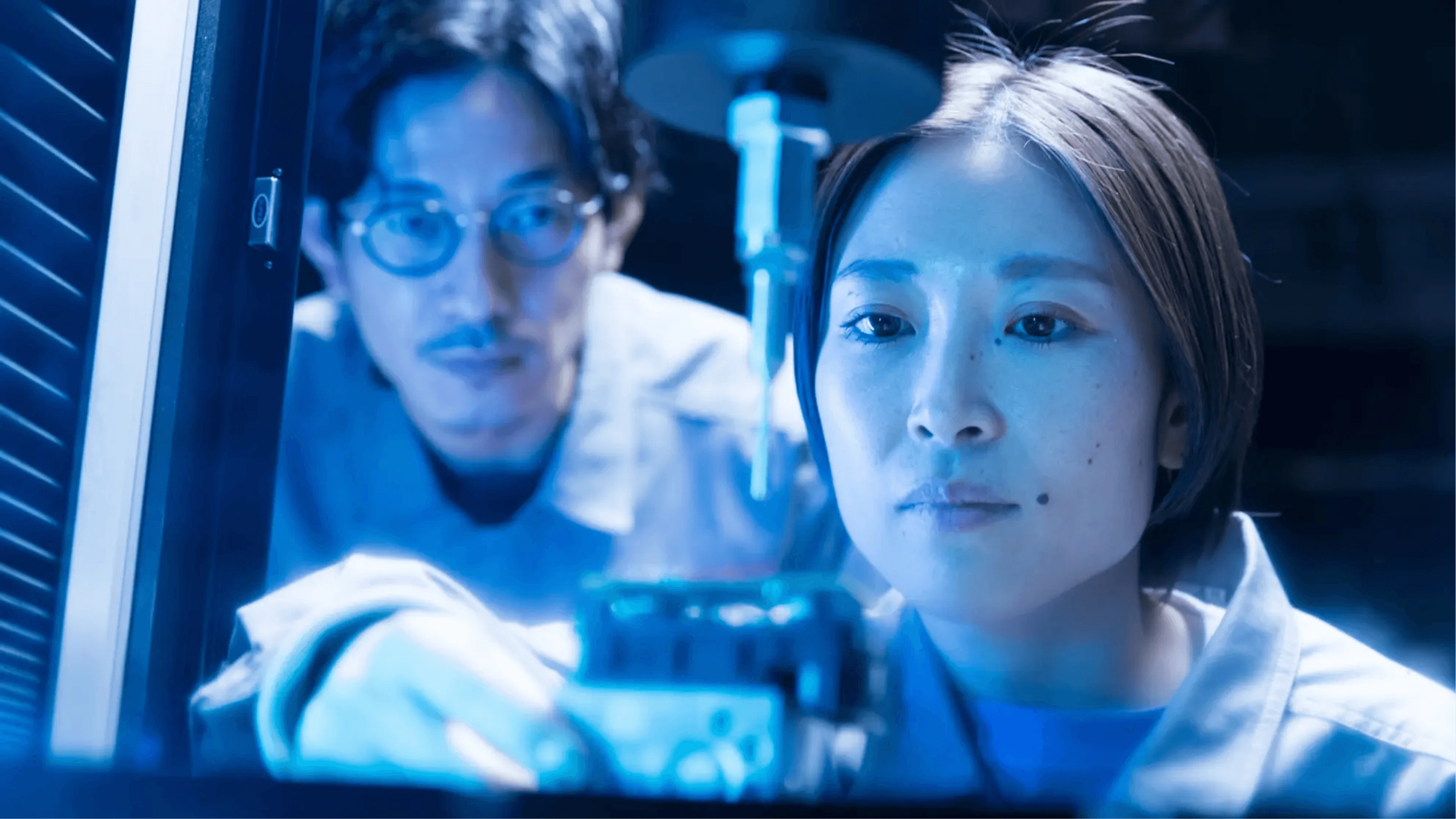 Two scientists working in a modern laboratory with blue ambient lighting and digital equipment, focused on their research.